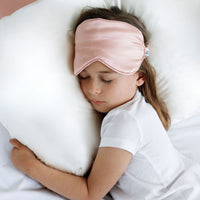 Child wearing a pink sleep mask while lying on a pillow