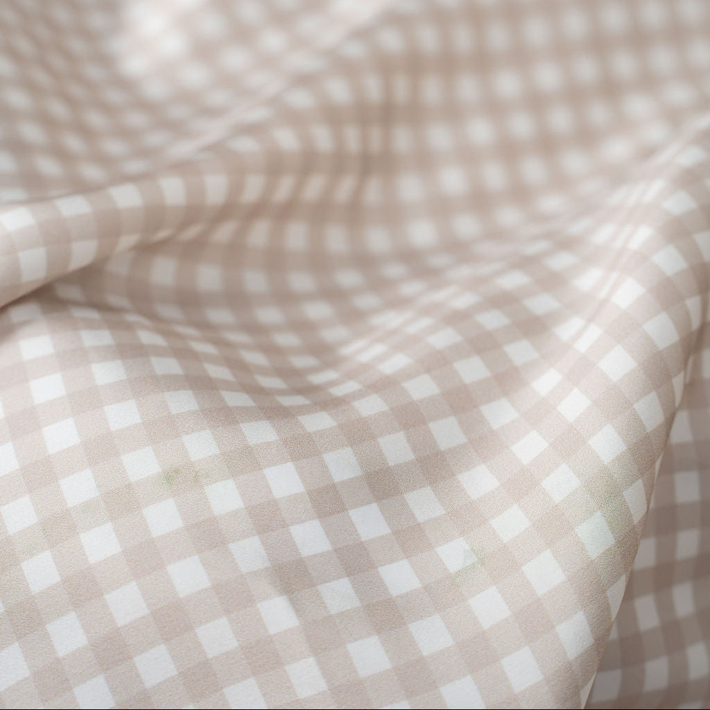 A close-up of draped fabric with a small gingham check pattern in warm beige and white.